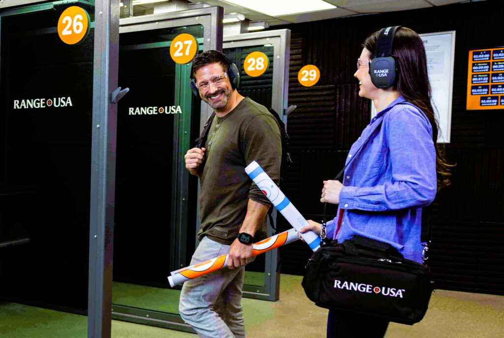 Man and a woman smile as they walk to their shooting lane at an indoor range.