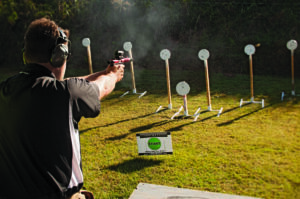 Man shooting at steel targets using a pistol topped with a red dot sight.